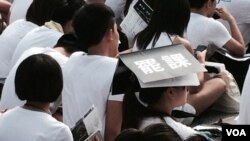 罷課學生在烈日下參與集會，有學生將大會提供的場刊放在頭上遮太陽。(美國之音湯惠芸)