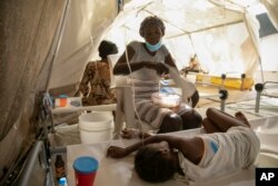 A woman uses a towel to swat flies away from her daughter stricken with cholera, at a clinic run by Doctors Without Borders in Port-au-Prince, Haiti, Friday, Nov. 11, 2022. (AP Photo/Odelyn Joseph)