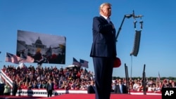 Mientras se muestran imágenes de fondo de la insurrección del 6 de enero de 2021 en el Capitolio de EE. UU., el expresidente Donald Trump se pone de pie mientras suena la canción "Justicia para todos" durante un mitin de campaña en Waco, Texas, el sábado 3 de marzo. 25, 2023.