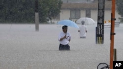 People wade through a street due to a heavy rain in Kurume, Fukuoka prefecture, southern Japan Monday, July 10, 2023.(Kyodo News via AP)