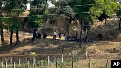 เจ้าหน้าที่ประจำชายแดนบังกลาเทศยืนเฝ้า สมาชิกหน่วยตำรวจตระเวณชายแดนเมียนมาในชุดเสื้อผ้าพลเรือน และนั่งหลบแดดใต้ต้นไม้ หลังละทิ้งหน้าที่ที่จุดผ่านแดน เพราะการต่อสู้ระหว่างกองทัพเมียนมาและกองทัพอาระกัน เมื่อวันที่ 5 ก.พ. 2567