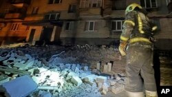 En esta fotografía proporcionada por el Servicio de Emergencia de Ucrania, un bombero examina los daños a un edificio de apartamentos tras un ataque con drones rusos en Dnipro, Ucrania, el 23 de febrero de 2024.