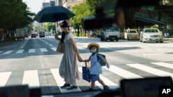 FILE - A pedestrian crossing a street with a child in Tokyo, Monday, July 19, 2021. The number of babies born in Japan last year fell for an eighth straight year to a new low, government data showed Tuesday, Feb. 27, 2024, (AP Photo/David Goldman, File)

