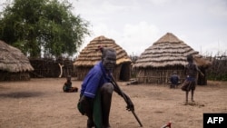 Mzee mmoja akiwa na watoto wake wamekaa nyumbani kwao huko Karamoja, Uganda, tarehe 24 Mei 2022. Picha na Badru KATUMBA/AFP.
