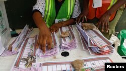 FILE - Electoral officials use stones to hold down ballots during the vote-counting process of the gubernatorial election at a polling unit in Lagos, Nigeria, March 18, 2023. 