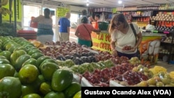 Una cliente revisa uvas, fresas y otras frutas exhibidas en un mercado de víveres en Maracaibo, en el occidente de Venezuela, mientras otros compradores se alistan para pagar sus pedidos, la mañana del jueves 13 de julio de 2023.