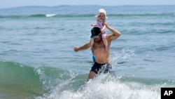 Jerome Quirion, de Sherbrooke, Quebec, Canadá, regresa a la orilla después de aventurarse en el frío océano Atlántico con su hija de 18 meses, Amelie, mientras estaba de vacaciones, en Old Orchard Beach, Maine, el martes 18 de junio de 2024.