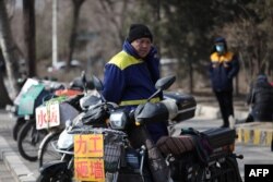 Seorang pekerja migran berdiri di samping poster yang mempromosikan keterampilan kerjanya di jalan saat menunggu untuk dipekerjakan di Shenyang, di Provinsi Liaoning, China Timur laut pada 25 Februari 2021. (Foto: AFP)