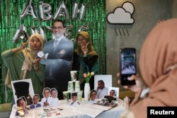 Perempuan berpose untuk foto dengan potongan foto calon Presiden Anies Baswedan saat Acara Humanies Cup Sleeve di kafe Kopi Nako di Jakarta, 4 Februari 2024. (REUTERS/Ajeng Dinar Ulfiana)