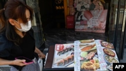 日本駐華大使館附近的一家日本餐廳前一名女子在看餐廳菜單。（2023年8月29日）