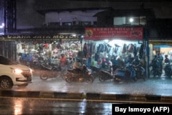 Pengendara sepeda motor berhenti di depan pertokoan pinggir jalan untuk berteduh dari hujan saat hujan deras di Jakarta pada 19 Januari 2022. (Foto: BAY ISMOYO/AFP)