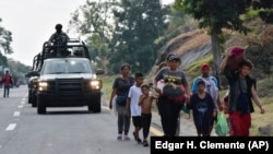 ARCHIVO - Un convoy de soldados de la Guardia Nacional pasa junto a migrantes que caminan hacia el norte por el costado de la carretera en Villa Comaltitlán, estado de Chiapas, sur de México, el 27 de diciembre de 2023.