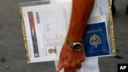 Un solicitante de visa estadounidense sostiene sus formularios del Departamento de Estado de Estados Unidos y su pasaporte cubano mientras espera en la fila frente a la entonces Sección de Intereses de EEUU -ahora embajada- en La Habana, el 1 de julio de 2015.