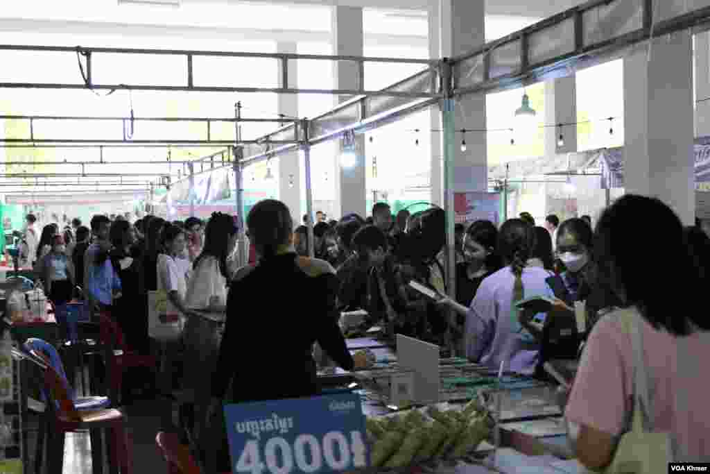 អ្នកចូលរួម​កំពុង​ឈរ​ទិញ​សៀវភៅ​ក្នុង​ស្តង់​សៀវភៅ​មួយកន្លែង​ក្នុង​កម្មវិធី​ពិព័រណ៌​សៀវភៅ​ក្នុង​ទិវា​ជាតិ​អំណាន​លើក​ទី​៩ នៅ​វិទ្យាស្ថានបច្ចេកវិទ្យាកម្ពុជា ក្នុង​រាជធានី​ភ្នំពេញ នាថ្ងៃទី​៩ ខែ​មីនា ឆ្នាំ​២០២៤។ (សើ ដាវី/វីអូអេ)