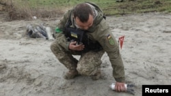 Seorang tentara pencari ranjau tampak mengambil serpihan bom tandan yang gagal meledak di area dekat desa Motyzhyn, di Kyiv, Ukraina, pada 10 April 2022. (Foto: Reuters/Mykola Tymchenko)