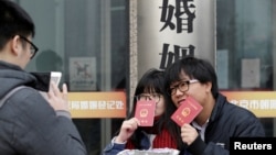 资料照：一对年轻人在北京一个婚姻登记处外手举结婚证留影。（2017年2月14日）
