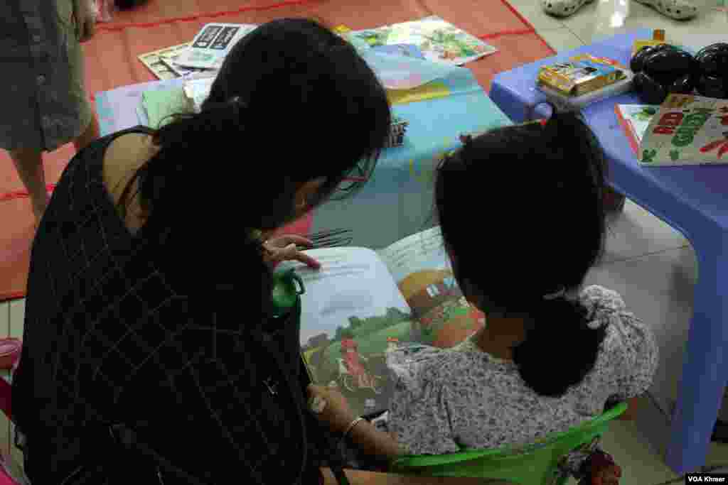 ស្ត្រី​ជា​ម្តាយ​មួយ​រូប​កំពុង​អាន​សៀវភៅ​ជាមួយ​កូនស្រី ក្នុង​កម្មវិធី​ពិព័រណ៌​សៀវភៅ​ក្នុង​ទិវា​ជាតិ​អំណាន​លើក​ទី​៩ នៅ​វិទ្យាស្ថានបច្ចេកវិទ្យាកម្ពុជា ក្នុង​រាជធានី​ភ្នំពេញ នាថ្ងៃទី​៩ ខែ​មីនា ឆ្នាំ​២០២៤។ (ស៊ឹម ចាន់សំណាង/វីអូអេ)