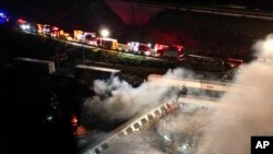 Asap terlihat keluar dari gerbong kereta di saat petugas pemadam kebakaran dan para tim evakuasi berusaha memadamkan api setelah tabrakan antar kereta terjadi di dekat Kota Larissa, di Yunani, pada 1 Maret 2023. (Foto: AP/Vaggelis Kousioras)