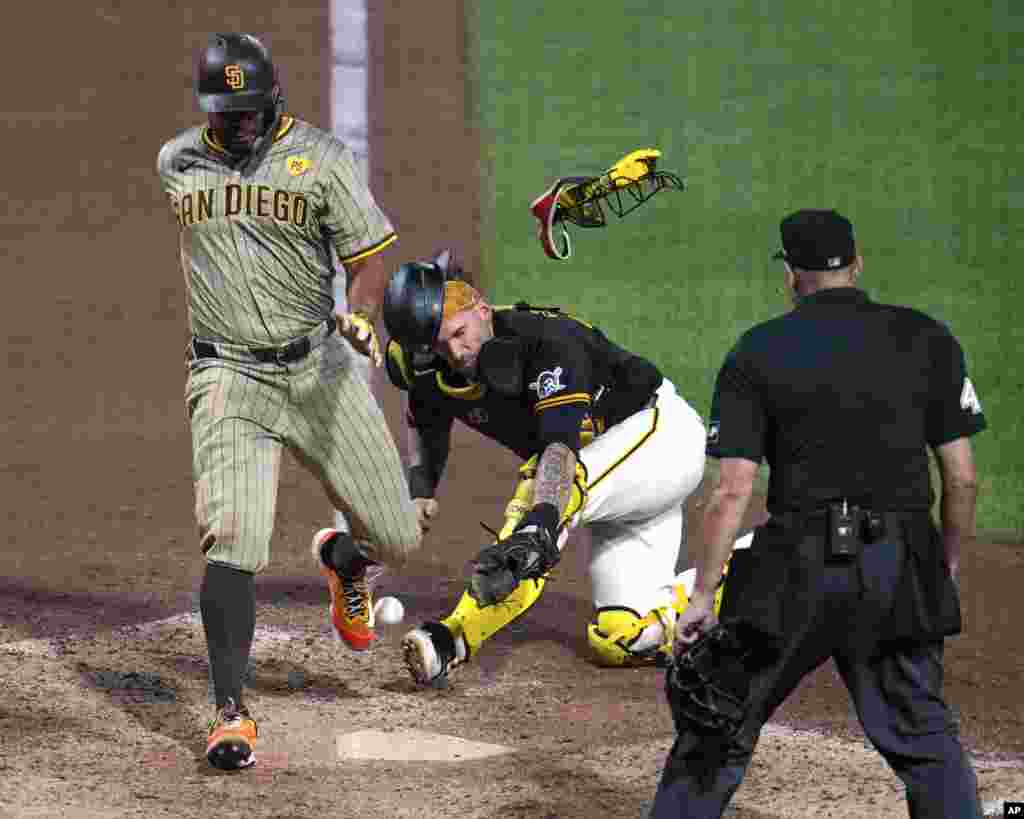 San Diego Padres' Xander Bogaerts, left, knocks the ball out of the glove of Pittsburgh Pirates catcher Yasmani Grandal, center, to score from third on a sacrifice fly by Jackson Merrill off relief pitcher Colin Holderman during the tenth inning of a baseball game in Pittsburgh, Pennsylvania, Aug. 7, 2024.