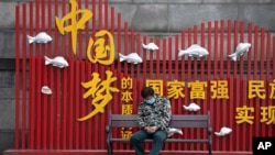 资料照：一名戴着口罩的男子在武汉街头一个中国梦的政府宣传牌下打盹。（2020年4月8日）