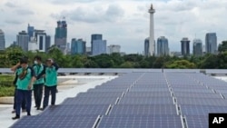 Para pekerja berjalan di dekat rangkaian panel surya penyedia sebagian energi listrik bagi Masjid Istiqlal, Jakarta. Renovasi besar-besaran pada tahun 2019 mencakup pemasangan 500 panel surya di atap masjid itu kini menjadi sumber energi bersih Istiqlal.