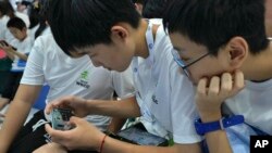 資料照片：2023年8月17日，在北京舉行的年度世界機器人大會上，一名學生幫助他的同學透過智慧型手機玩網路遊戲。 （美聯社照片）