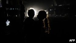 Seorang gadis Palestina menggendong seorang anak terlihat di depan lampu mobil yang melaju di Rafah, di Jalur Gaza selatan pada 4 Mei 2024, di tengah konflik antara Israel dan kelompok militan Hamas. (Foto: AFP)