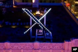 Para pekerja memasang penerangan pada tanda "X" di atas kantor pusat perusahaan, yang sebelumnya dikenal sebagai Twitter, di San Francisco, pada 28 Juli 2023. (Foto: AP)