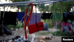 El teléfono celular de un solicitante de asilo cuelga mientras recarga la batería, a la espera de cruzar a EEUU con una cita a través de la aplicación de Aduanas y Protección Fronteriza, en un campamento improvisado en Matamoros, México, el 21 de junio de 2023.
