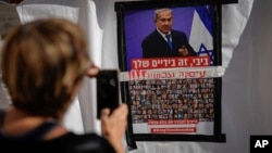 以色列特拉维夫的一名女子用手机拍摄的一张海报照片显示，内塔尼亚胡总理照片下贴有被关押在加沙的以色列人质的照片，海报要求以色列领导人达成协议将人质带回家。（2023年11月21日）
