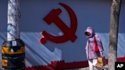 一名女子走过北京一处住宅小区围墙上的中共标识。（2024年3月1日）