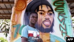 Le peintre ivoirien Lopoa Kouassi Bi "LK" pose pour un portrait devant un "Massa", un taxi partagé décoré, à Yamoussoukro le 25 janvier 2024.