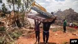 Watu wawili wakibeba magodoro baada ya mlima wa taka kuporomoka mjini Kampala, Agosti 10, 2024. Picha ya AFP