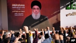 Pendukung kelompok Hizbullah yang didukung Iran mengacungkan tinju dan bersorak ketika pemimpin Hizbullah Sayyed Hassan Nasrallah muncul melalui tautan video selama rapat umum di Beirut, Lebanon hari Jumat, 3 November 2023.