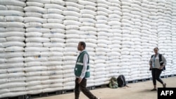 Wafanyakazi wa Shirika la Mpango wa Chakula Duniani (WFP) wakipita mbele ya magunia ya ngano yaliyokuwa kwenye ghala huko Adama, Ethiopia, Januari 12, 2023. Picha na Amanuel Sileshi / AFP.