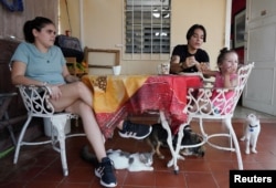 La pareja conformada por Gabriela Alfonso Pérez, de 23 años, y Ria Acosta, de 27, conversan en una mesa en su jardín junto con la hija de Ria, Ivelle Acosta, de 2 años, en La Habana, Cuba, el 13 de julio de 2022.