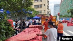 中国广东深圳的工人正在准备给一住宅小区外竖立围栏，与此同时小区居民正在排队做核酸。（2022年8月29日）