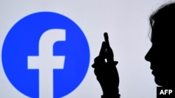 FILE - In this photo illustration, a person looks at a smartphone with a Facebook App logo displayed on the background, on Aug. 17, 2021.
