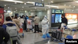 Passengers arriving on international flights wait in line next to a staff member wearing personal protective equipment (PPE) at the airport in Chengdu, China, Jan. 6, 2023. 
