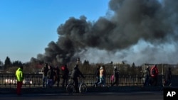 មនុស្ស​ដើរ​ក្បែរ​តំបន់​មួយ​ដែល​មាន​ផ្សែង​ហុយ​យ៉ាង​ខ្លាំង​ក្រោយ​ពី​មាន​ការ​ផ្ទុះ​នៅ​ជិត​ព្រលាន​យន្តហោះ​នៅ​ជិត​ក្រុង​ Lviv ភាគ​ខាង​លិច​ប្រទេស​អ៊ុយក្រែន កាល​ពី​ថ្ងៃ​ទី​១៨ ខែ​មីនា ឆ្នាំ​២០២២។