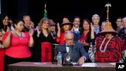 Washington Gov. Jay Inslee, center, reaches for a pen as tribal leaders and other supporters applaud the signing of a bill that creates a first-in-the-nation statewide alert system for missing Indigenous people, in Quil Ceda Village, near Marysville, Wash., March 31, 2022. 