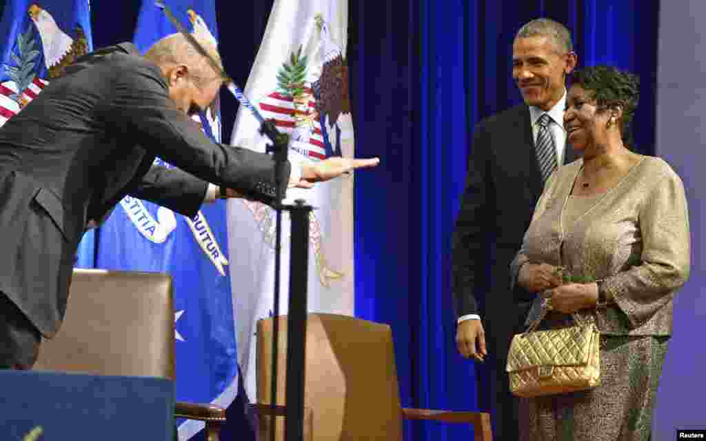 U.S. President Barack Obama (R) escorts singer Aretha Franklin as Attorney General Eric Holder (L) bows in surprise after the unveiling of Holder's official portrait at the Dept. of Justice, in Washington, Feb. 27, 2015.