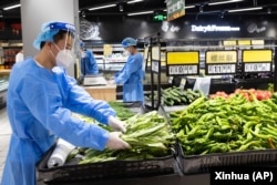 中共官媒新华社发布照片显示身穿防护服的人员在上海徐汇区超市里出售蔬菜。（2022年5月16日）
