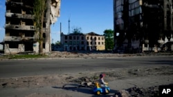 Dečak se igra ispred zgrada uništenih u bombardovanju, u Borođanki, Ukrajina, 24. maja 2022.