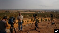 FILE - TV reporters work on a hilltop on the Turkey-Syria border overlooking Ras al-Ayn in northeastern Syria, Oct. 20, 2019. Journalists in northeastern Syria now face a requirement to join an official union before being credentialed.