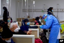 In this photo released by Xinhua News Agency, a medical worker helps a patient on an intravenous drip at a community health care institution in Shanghai, China, Jan. 5, 2023.