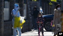 Una niña con una máscara facial y montada en un scooter pasa junto a un trabajador con traje protector que se dirigía a recolectar muestras de COVID de los residentes encerrados en Beijing, el 1 de diciembre de 2022.