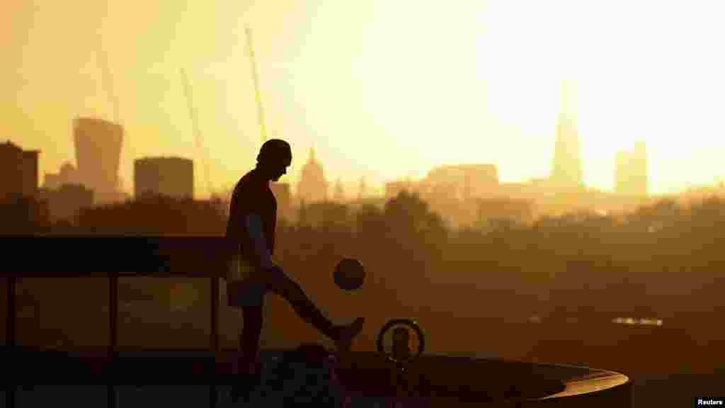 A person films himself doing kick-ups with a football during sunrise on Primrose Hill in London.