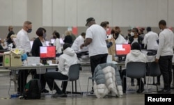 Wafanyakazi wa uchaguzi wakiweka kura zilizopigwa kwa njia ya posta katika mashine ya kuhesabu kura wakati wa uchaguzi wa katikati ya muhula huko Huntington Place, Detroit, Michigan, Marekani Novemba 8, 2022. REUTERS/Rebecca Cook