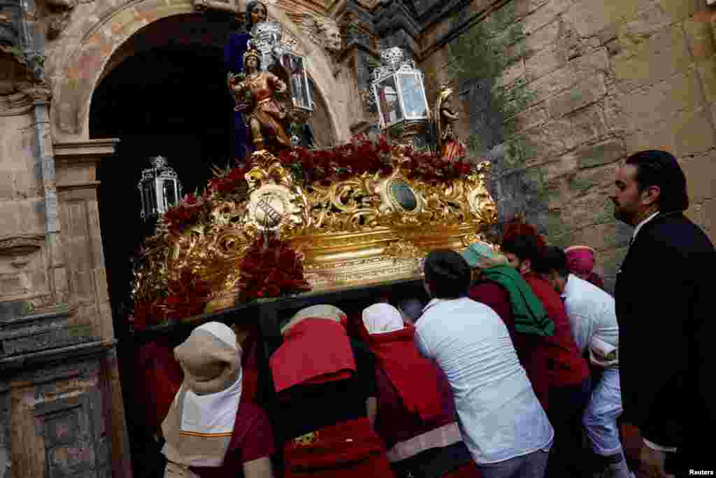 Costaleros pertenecientes a la hermandad de Los Gitanos salen de una iglesia mientras llevan una estatua de Cristo en una estructura conocida tradicionalmente como 'paso'.